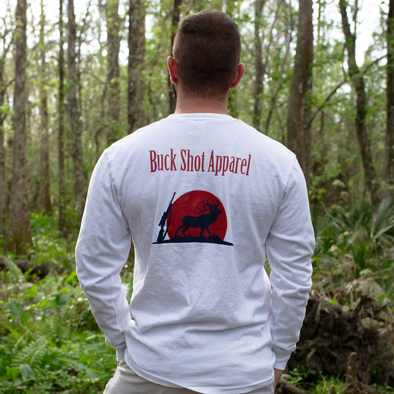 A man standing in the woods wearing a long sleeve shirt.