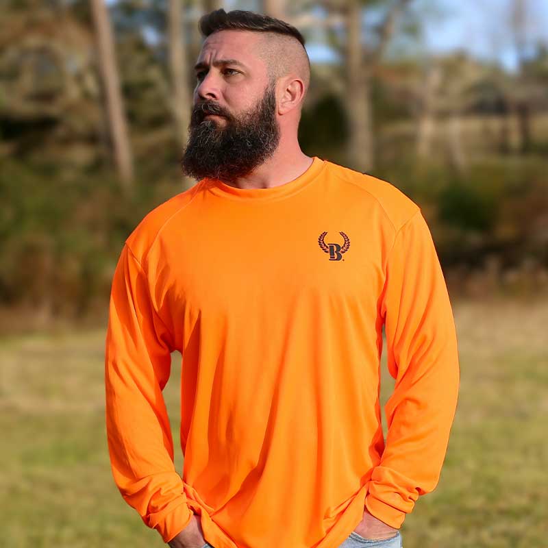 A man standing in the grass wearing an orange shirt.