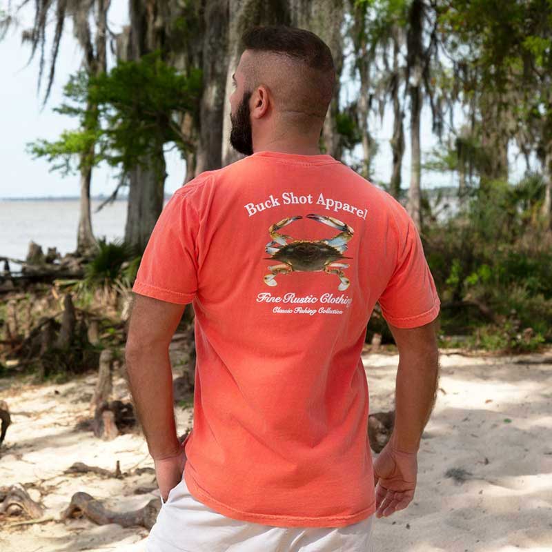 A man standing on the beach wearing a coral shirt.