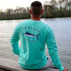 A man sitting on the dock of a lake wearing a long sleeve shirt.