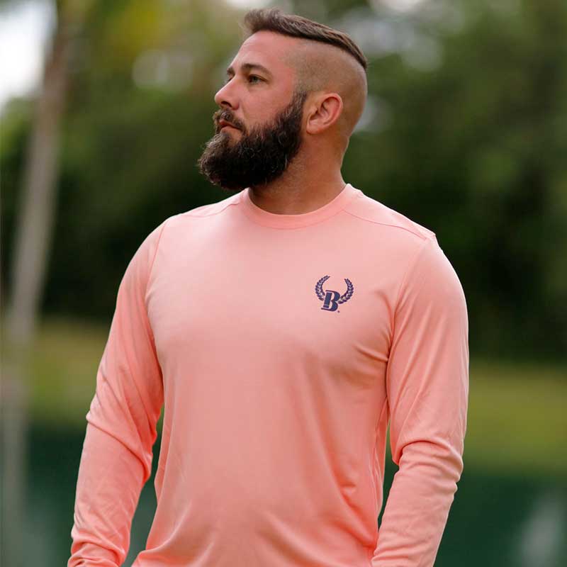 A man with a shaved head and beard wearing a pink shirt.