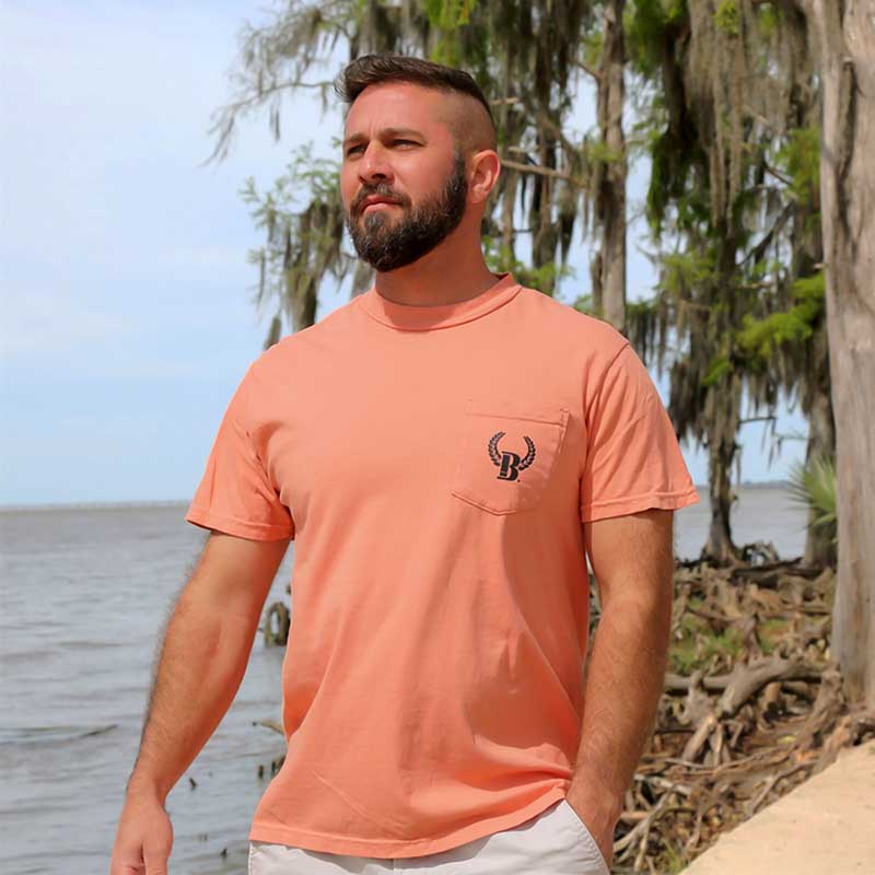 A man standing on the beach wearing an orange shirt.