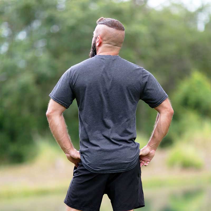 A man with a shaved head and a beard is standing in the grass.