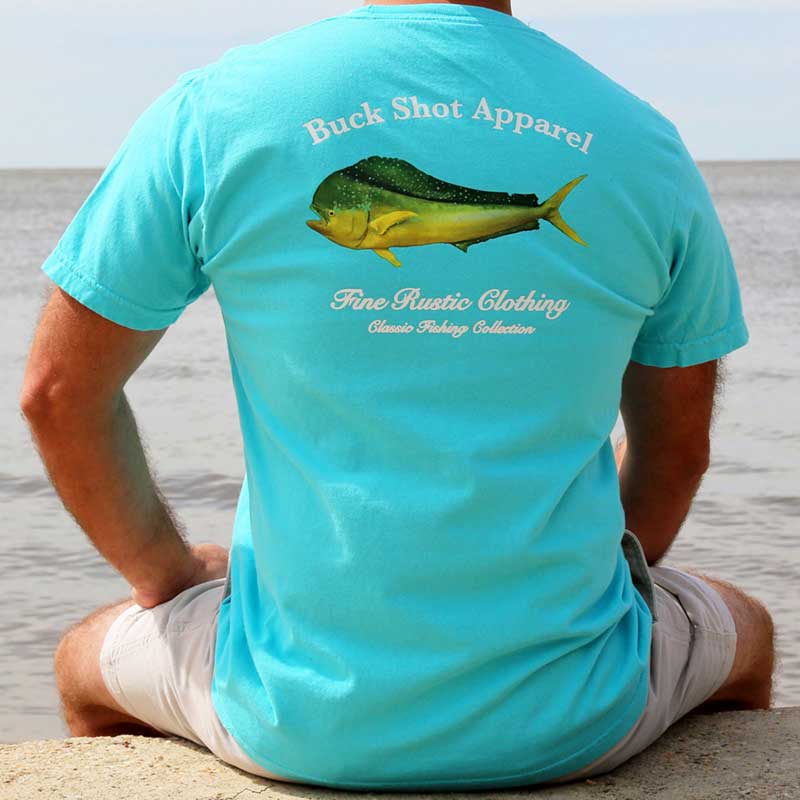 A man sitting on the beach wearing a t-shirt with an image of a fish.