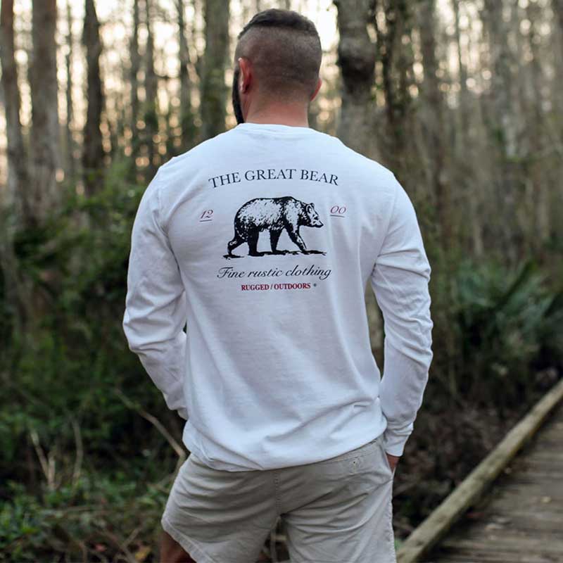 A man standing in the woods wearing shorts and a long sleeve shirt.