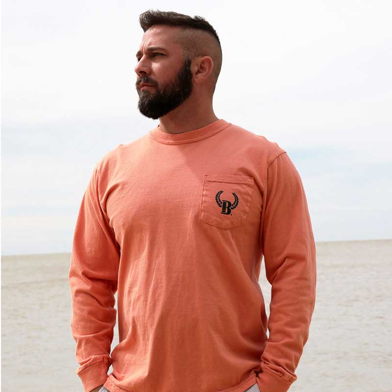 A man with a shaved head and beard standing on the beach.