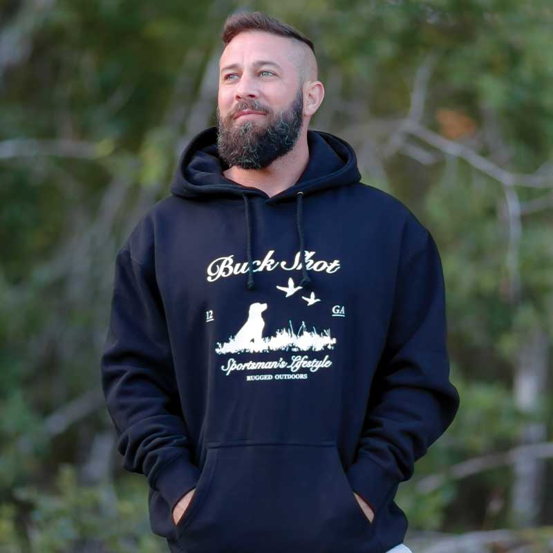 A man standing in front of some trees wearing a black hoodie.