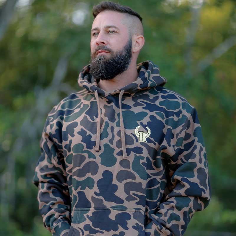 A man with a beard and mustache wearing a camo hoodie.