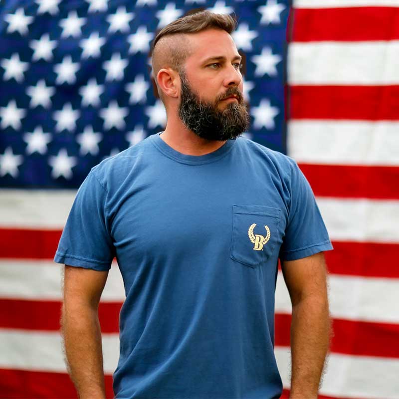 A man with a beard and mustache standing in front of an american flag.