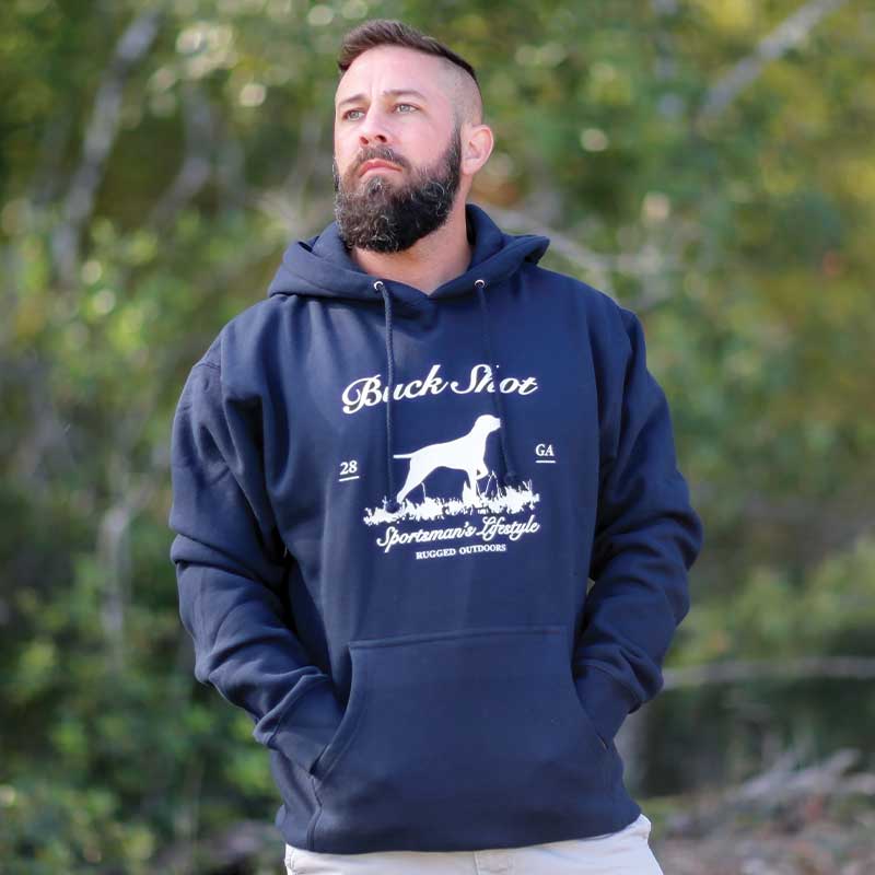 A man standing in front of some trees wearing a hoodie