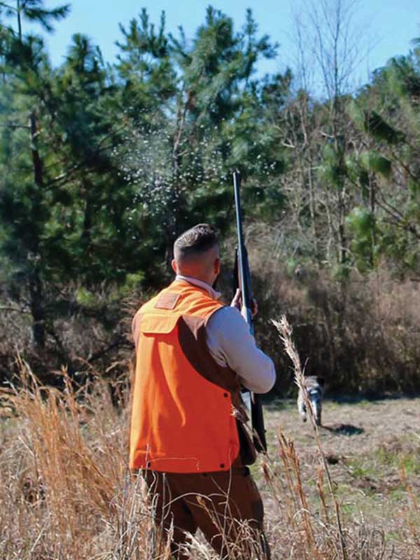 A man in an orange vest holding a gun.