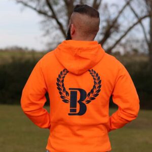 A man standing in the grass wearing an orange hoodie.