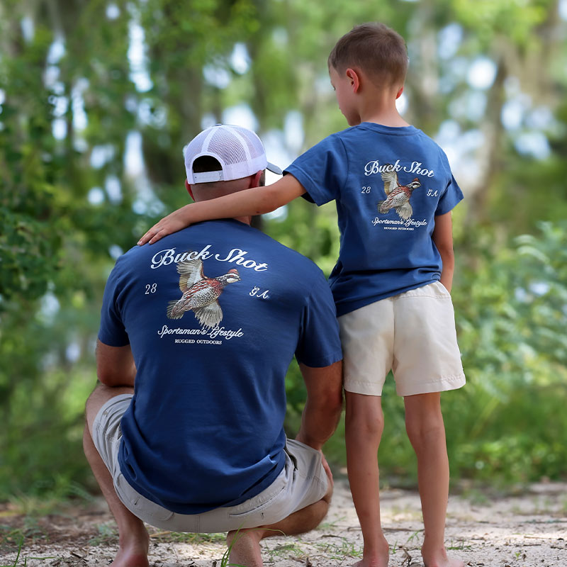 Father and Son-Quail back Father and youth wearing matching t-shirts featuring a Bobwhite Quail graphic with son's arm around dad's shoulder
