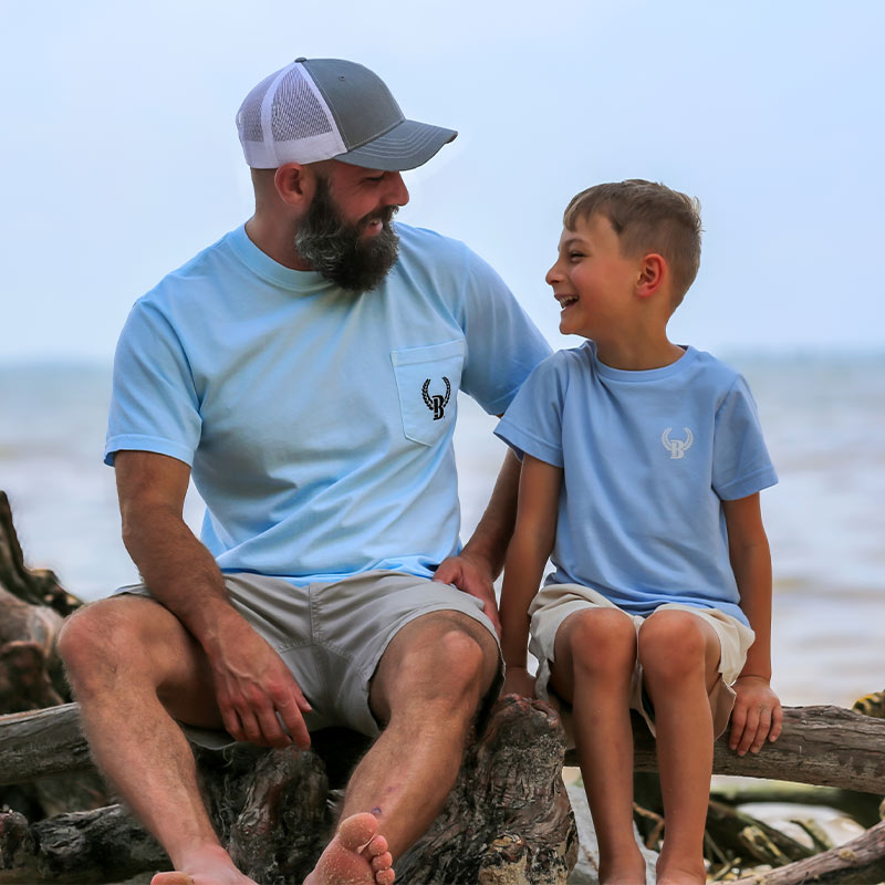 father-&-son Crappie front Father and son wearing matching t-shirts sitting on driftwood by the lake